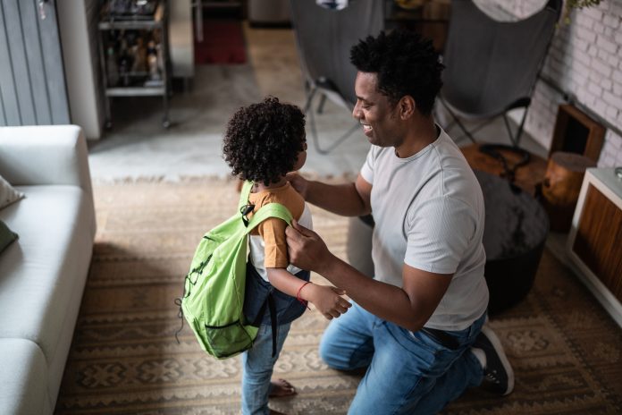 Father helping son with backpack at home before leaving to school, school readiness