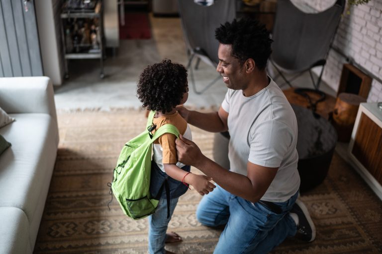Father helping son with backpack at home before leaving to school, school readiness