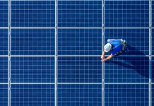 Male engineer in blue suit and protective helmet installing photovoltaic panel system. Professional electrician mounting solar module on roof. Alternative energy ecological concept