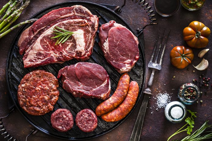 Various cuts of raw meat shot from above on a cast iron grill