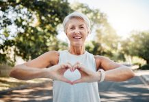 Fitness, happy and heart hands of old woman in nature after running for health, wellness and workout. Smile, motivation and peace with senior lady and sign for love, faith and training in nature