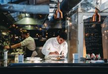 A chef is cooking in his restaurant's kitchen. Shot through the glass. High-end gourmet restaurant.