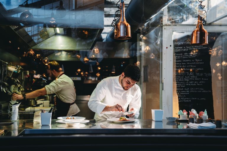 A chef is cooking in his restaurant's kitchen. Shot through the glass. High-end gourmet restaurant.