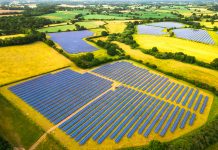 Aerial view, taken by drone, of a solar farm - and many banks of solar panels in a row - in the heart of the rural landscape of southeast England.