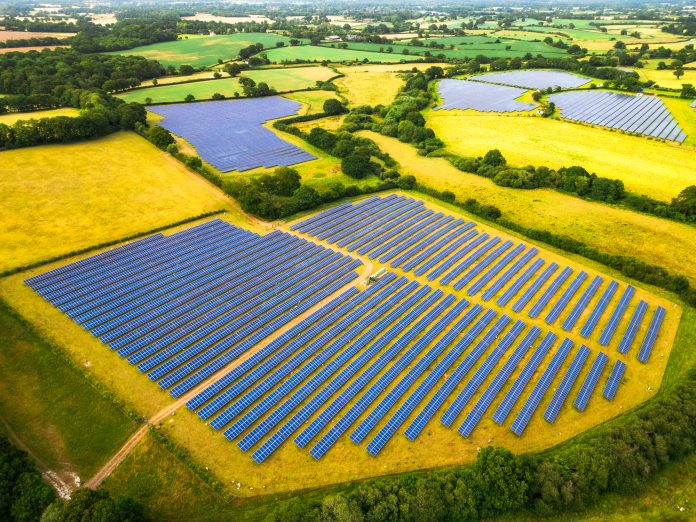 Aerial view, taken by drone, of a solar farm - and many banks of solar panels in a row - in the heart of the rural landscape of southeast England.