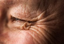 A middle-aged, blue-eyed, Caucasian person's eye looks to the side while smiling with wrinkled skin.