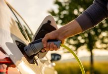 Man inserts a power cord into an electric car for charging in the nature