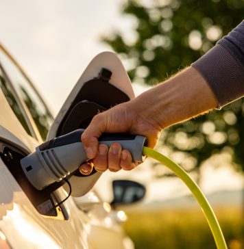 Man inserts a power cord into an electric car for charging in the nature