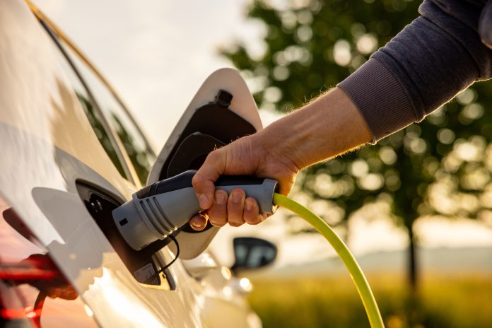 Man inserts a power cord into an electric car for charging in the nature