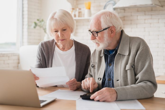 Serious caucasian old elderly senior couple grandparents family counting funds on calculator, doing paperwork, savings, paying domestic bills, mortgage loan, pension at home using laptop.