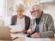 Serious caucasian old elderly senior couple grandparents family counting funds on calculator, doing paperwork, savings, paying domestic bills, mortgage loan, pension at home using laptop.