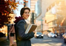 Young happy female student standing on the street and looking at camera.