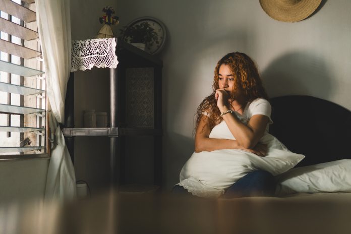 Young Latin American woman sitting in her room biting her fingers. anxiety concept