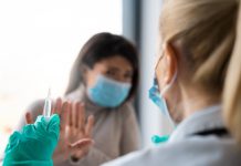 A female patient is refusing to take a shot from her doctor. She is holding her hands in front of her doctor as if defending herself from the syringe and the needle.