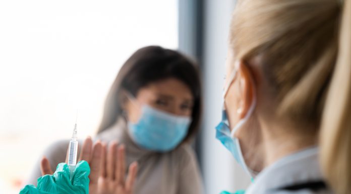 A female patient is refusing to take a shot from her doctor. She is holding her hands in front of her doctor as if defending herself from the syringe and the needle.