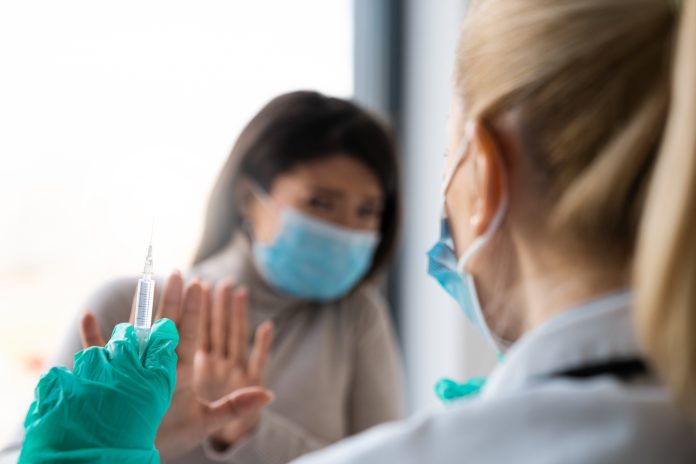 A female patient is refusing to take a shot from her doctor. She is holding her hands in front of her doctor as if defending herself from the syringe and the needle.