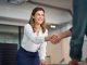 Happy mid aged business woman manager handshaking greeting client in office. Smiling female executive making successful deal with partner shaking hand at work standing at meeting table.