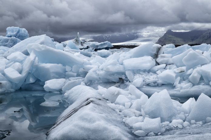 Blue icebergs floating the glacial lagoon in southeast Iceland in summer, blue water in the foreground with copy space and mountains and glacier in the background.