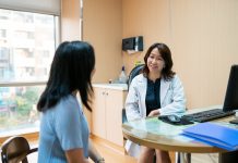 Smiling female doctor talking to patient. Mature healthcare worker is discussing with woman. They are sitting in clinic.