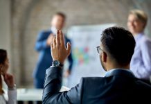 Rear view of a businessman raising his hand to ask the question during business presentation in the office.