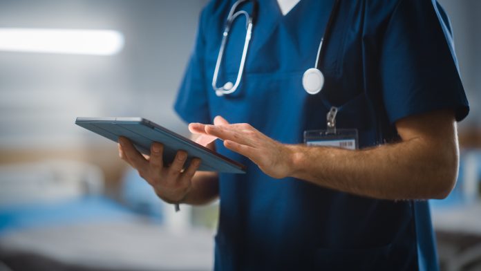 Hospital Ward: Unrecognizable Head Nurse, Doctor, Surgeon Uses Digital Tablet Computer Health Care Vitals Monitoring Computer Machine. Modern Clinic with Advanced Equipment and Professional Working