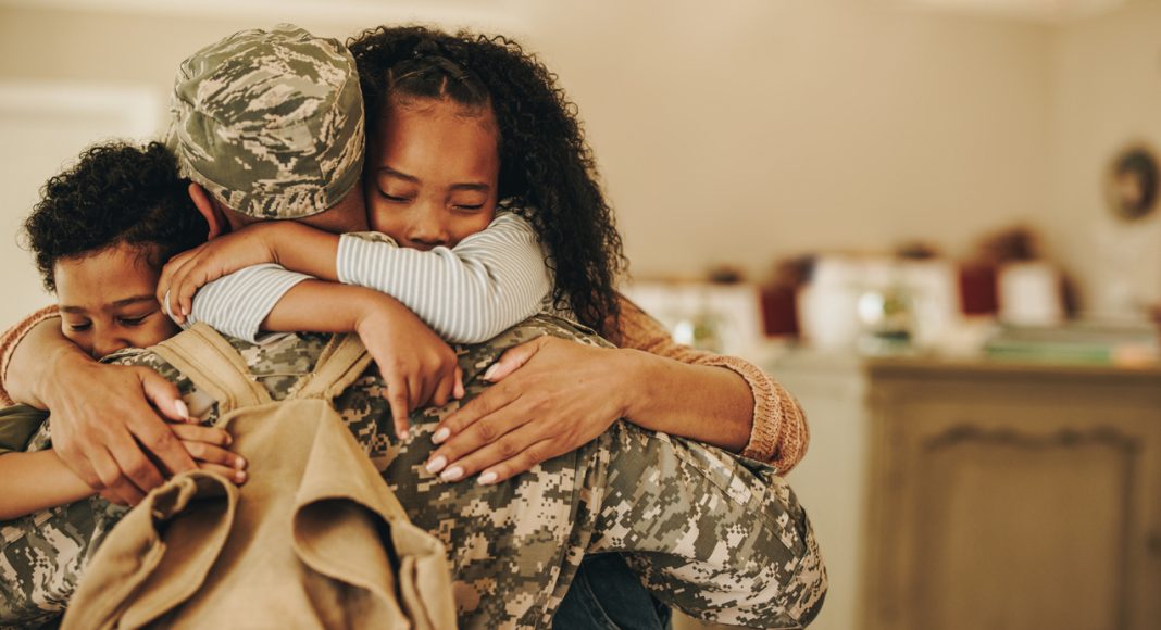 Soldier embracing his wife and kids on his homecoming. Serviceman receiving a warm welcome from his family after returning from deployment. Military family having an emotional reunion.