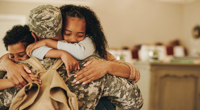 Soldier embracing his wife and kids on his homecoming. Serviceman receiving a warm welcome from his family after returning from deployment. Military family having an emotional reunion.