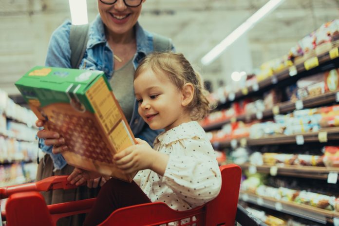 Portrait of a Young Girl Holding a Box of Cereal While Shopping With Mom at the Supermarket