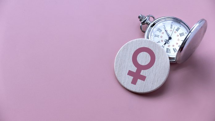 Menopause concept. Women symbol over a watch. Healthcare and medical for women. Pink background with copy space.