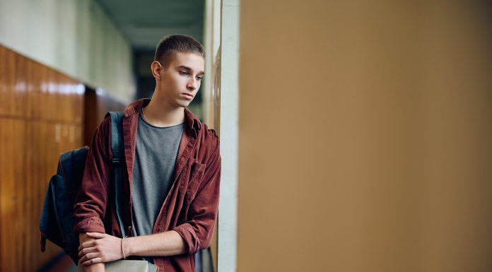 Sad teenage boy thinking of something while standing in hallway at high school. Copy space. article covering: Right-wing ethno-nationalists and jihadi Salafists