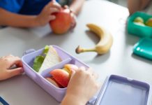 School kids eating healthy food from packed lunch boxes. Children at table in cafeteria. Pupils have vegetarian breakfast in canteen. Back to school concept. Lifestyle moment in elementary college