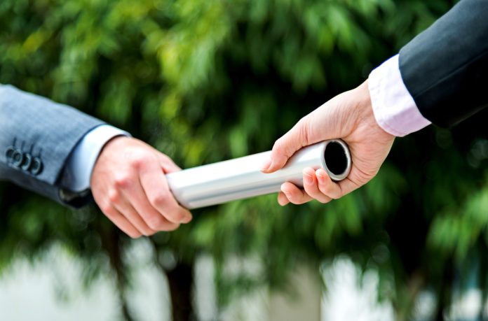 Businesswoman passing baton to a businesswoman outdoors.