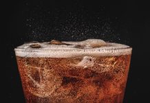 close up ice cola in glass and bubble soda splashing on black background