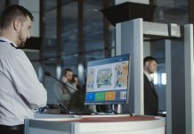 Man in uniform standing at counter at checking point and watching at monitor with x-ray of luggage.