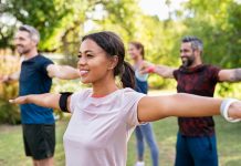 Group of multiethnic mature people stretching arms outdoor. Middle aged yoga class doing breathing exercise at park. Beautifil women and fit men doing breath exercise together with outstretched arms.