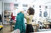 Skilled experienced worker or fashion designer in a professional atelier smiling while standing in front of a mannequin with a tape measure on her neck.