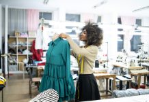 Skilled experienced worker or fashion designer in a professional atelier smiling while standing in front of a mannequin with a tape measure on her neck.