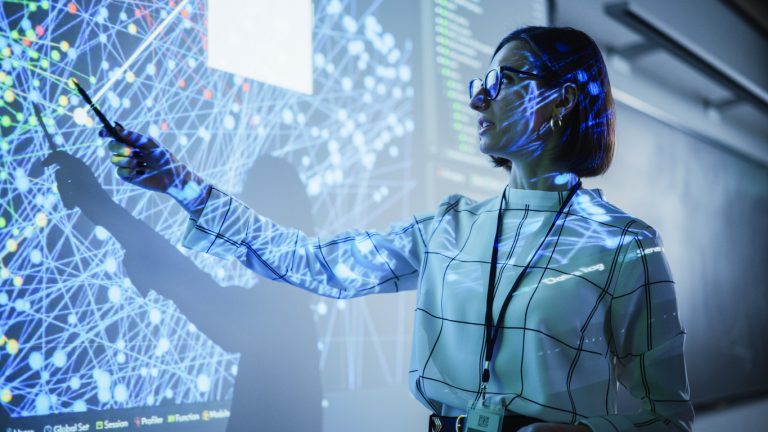 Young Female Teacher Giving a Data Science Presentation in a Dark Auditorium with Projecting Slideshow with Artificial Intelligence Neural Network Architecture. Business Startup and Education Concept