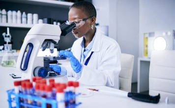 Science, laboratory and woman on microscope for blood test research, medical analysis and dna or virus tube. Biotechnology, healthcare and scientist, doctor or african person check for particles