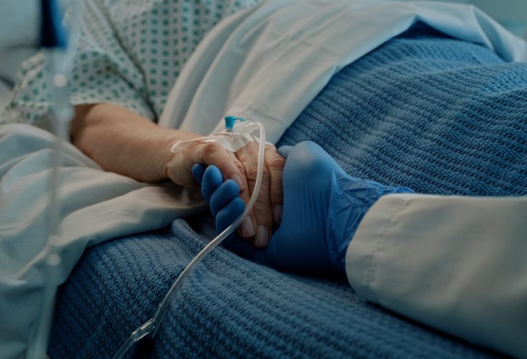 Hospital, holding hands and bed with doctor, support and care together in a clinic after surgery. Senior, healthcare and cancer patient with empathy, kindness and caregiver with compassion with help