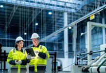 Male and female engineers in neat work clothes prepare and control the production system of large modern machines in a factory producing industrial technology products.