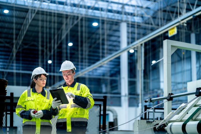 Male and female engineers in neat work clothes prepare and control the production system of large modern machines in a factory producing industrial technology products.