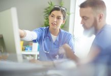 young medical professional discussing notes with her colleague at her desk .