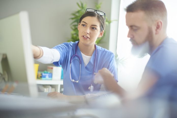 young medical professional discussing notes with her colleague at her desk .