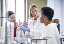 Mature chemistry teacher holding molecular model, students listening