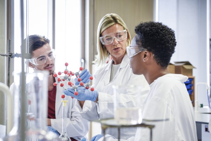 Mature chemistry teacher holding molecular model, students listening