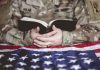 An American soldier mourning and praying with the Bible in his hands and the American flag