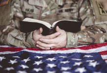 An American soldier mourning and praying with the Bible in his hands and the American flag