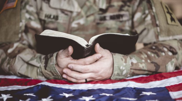 An American soldier mourning and praying with the Bible in his hands and the American flag