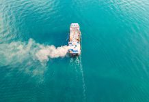 Aerial view of a container ship carrying cargo for an import-export logistics business in the ocean. Smoke from a ship sailing in the ocean